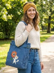 blue canvas tote bag featuring a cute white cat holding an orange sunflower embroidery, with side pockets and adjustable brass buckle straps