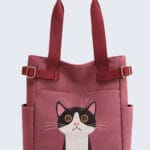 Embroidered tuxedo cat tote bag in burgundy with side pockets. Quirky cat-themed canvas handbag with adjustable straps for cat lovers.