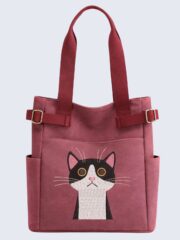 Embroidered tuxedo cat tote bag in burgundy with side pockets. Quirky cat-themed canvas handbag with adjustable straps for cat lovers.