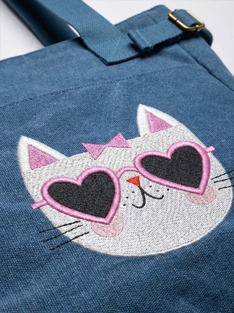 Macro shot of the intricate thread work and texture of the Hipster Kitty embroidery on a durable blue tote