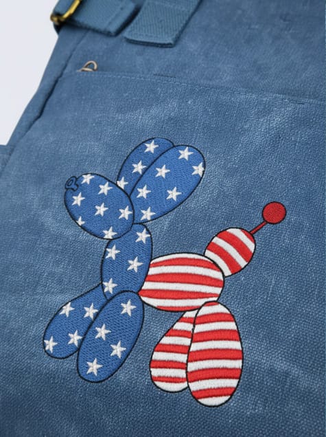 Close-up of high-quality embroidery on a blue fabric, showing intricate white stars on blue and red stripes on white in the shape of a balloon dog.