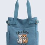 Front view of a blue canvas tote bag featuring "Life is Better with Cats" embroidery with two cute cartoon cats, an ideal gift for cat lovers.