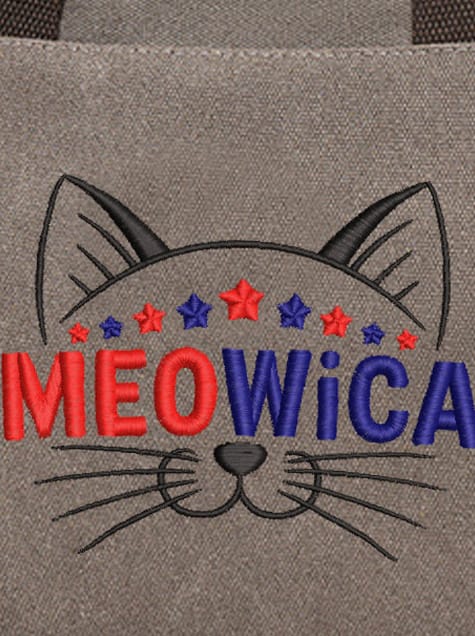 A close-up of a gray canvas fabric featuring an embroidery design of a black-outlined cat face. The word MEOWiCA is stitched across the center in bold red and blue letters, topped with a row of alternating red and blue stars. The cat's features include pointed ears, whiskers, and a small black nose.